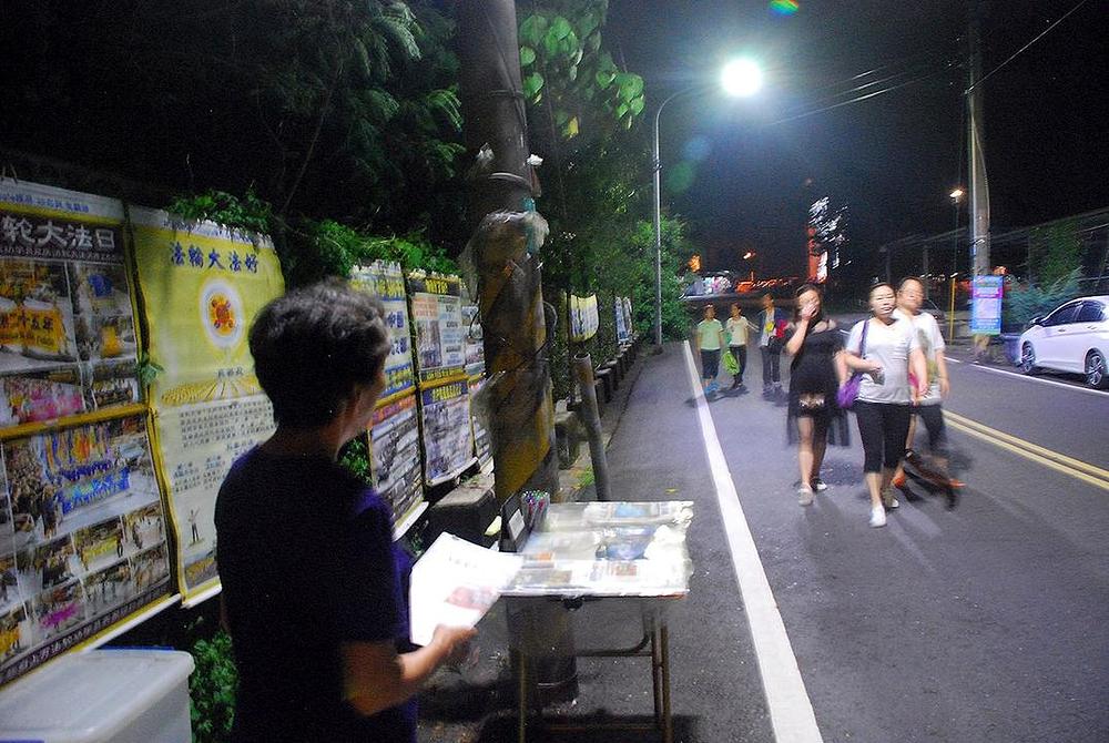 Grupe turista iz matice Kine šetaju prema brani nakon večere, prolazeći pored izložbenih panela koje su postavili Falun Dafa praktikanti.
