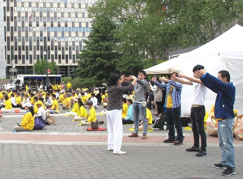 Gledajući izvođenje Falun Dafa vježbi, pješaci probaju pokrete vježbi.
