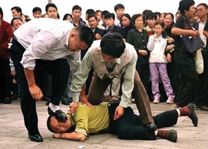  Na trgu Tiananmen, naočigled mnogih promatrača, policajac u civilu staje na lice nenaoružanog Falun Gong praktikanta, dok drugi policajac staje čovjeku na nogu i stavlja mu lisice na vrat. (Fotografija: The Associated Press)