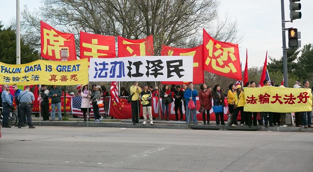  Praktikanti Falun Gonga drže transparent ispred hotela u kom je Xi odsjeo. Ne bijelom transparentu piše: „Privedite Jianga pred lice pravde“