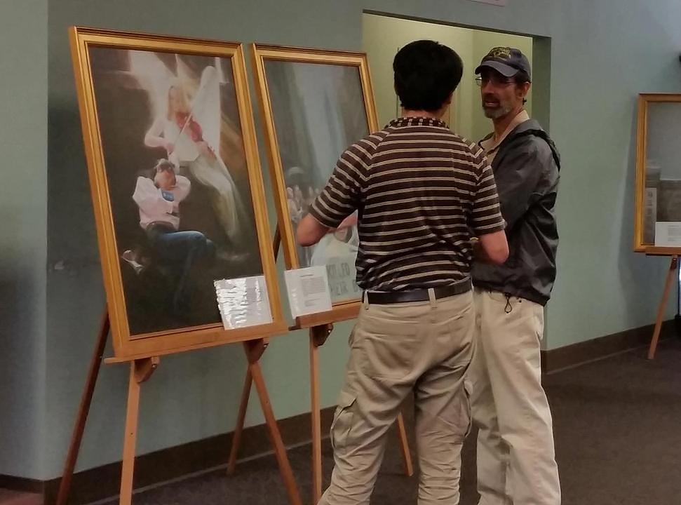 Lokalni umjetnik diskutuje o slikama sa volonterom na izložbi.