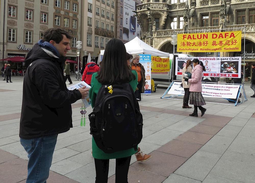 Praktikant razgovaraj sa prolaznicom ispred Falun Gong plakata na Marienplatzu.