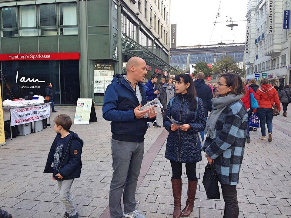 Prolaznici od praktikanata slušaju o Falun Gongu.