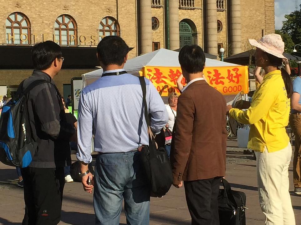 Kineski turisti zastaju kako bi gledali Falun Gong aktivnosti.